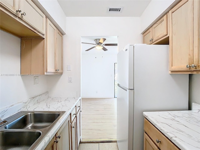 kitchen with light brown cabinetry, sink, white refrigerator, ceiling fan, and light hardwood / wood-style floors