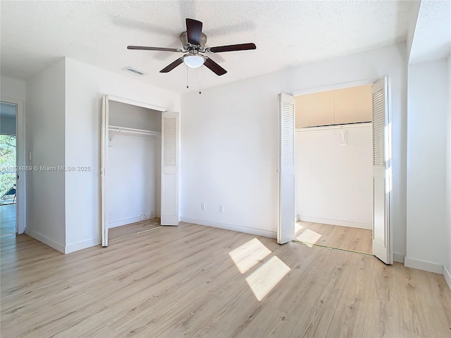 unfurnished bedroom with multiple closets, ceiling fan, light hardwood / wood-style flooring, and a textured ceiling