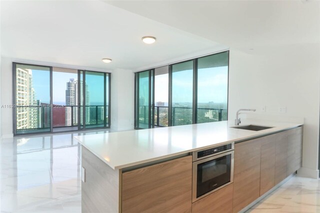 kitchen featuring expansive windows, sink, stainless steel oven, and kitchen peninsula