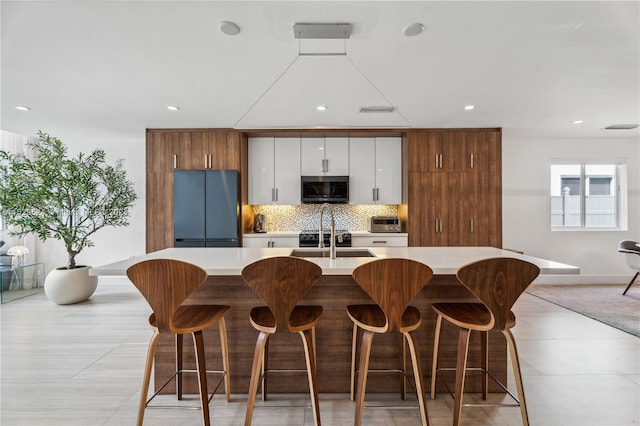 kitchen featuring a breakfast bar area, stainless steel appliances, a center island with sink, sink, and white cabinets