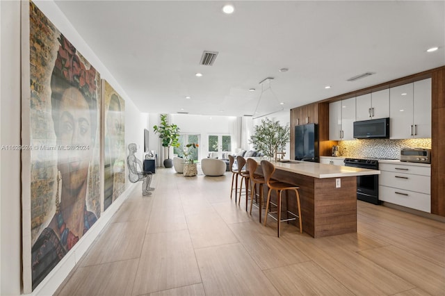 kitchen featuring a breakfast bar area, black appliances, a center island, and white cabinets