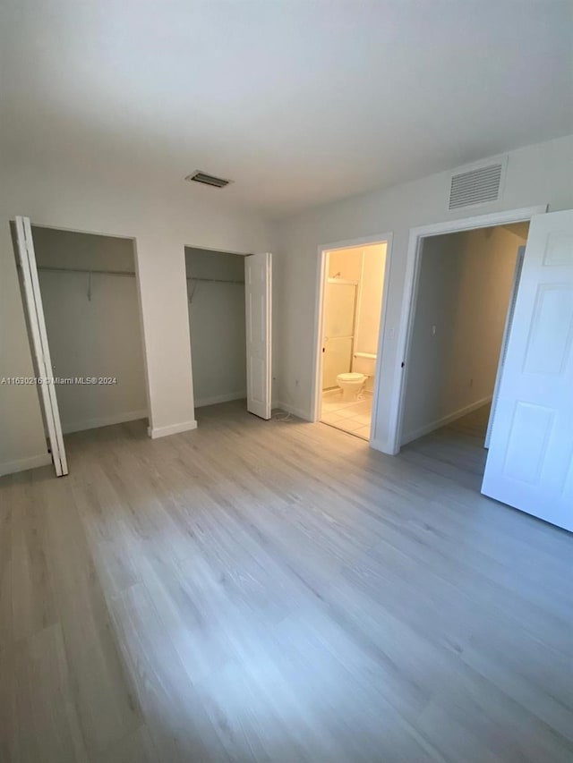 unfurnished bedroom featuring connected bathroom, two closets, and light hardwood / wood-style floors