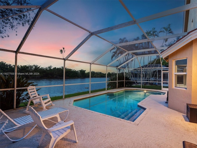 pool at dusk featuring a lanai, a water view, and a patio