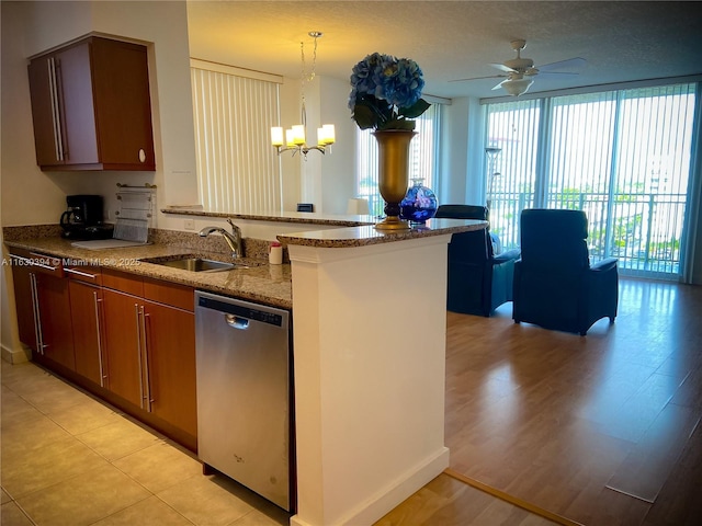 kitchen featuring light stone counters, a peninsula, a sink, stainless steel dishwasher, and brown cabinetry