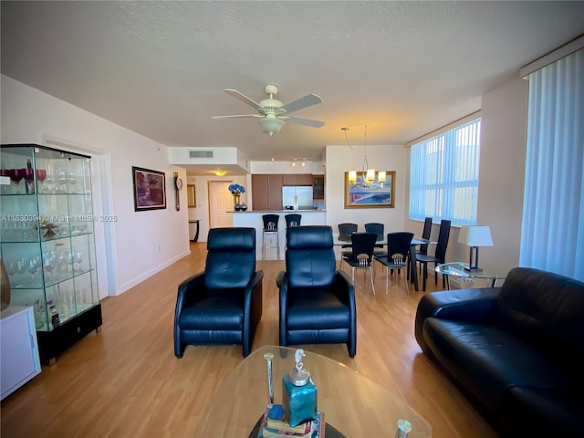 living room featuring light wood-type flooring, visible vents, a textured ceiling, and ceiling fan with notable chandelier