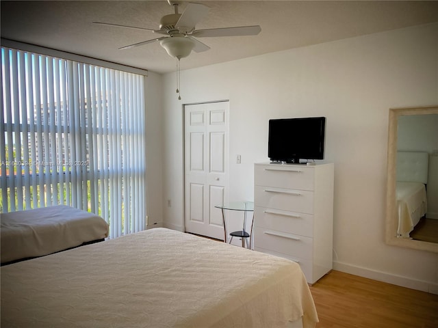 bedroom featuring ceiling fan, a closet, light wood-style flooring, and baseboards