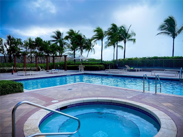 community pool with a patio area, fence, and a hot tub