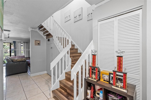 staircase featuring crown molding, tile patterned flooring, and a textured ceiling