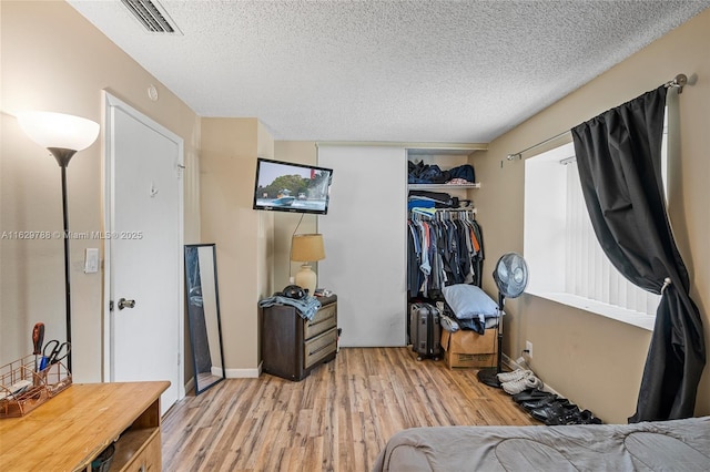 bedroom with a textured ceiling, light wood-type flooring, and a closet