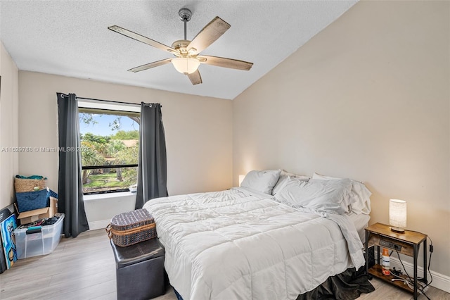 bedroom with lofted ceiling, a textured ceiling, ceiling fan, and light hardwood / wood-style flooring