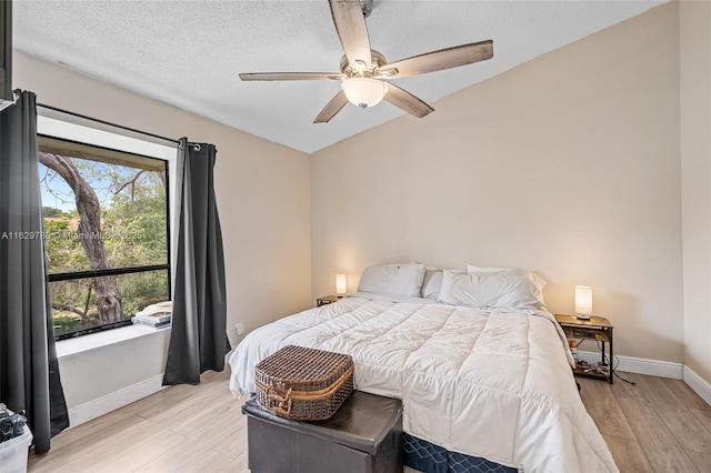 bedroom featuring lofted ceiling, light wood-type flooring, ceiling fan, and a textured ceiling