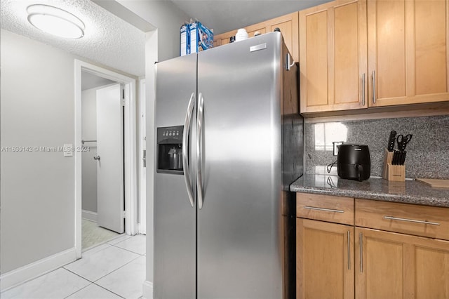 kitchen featuring stainless steel refrigerator with ice dispenser, backsplash, dark stone counters, a textured ceiling, and light tile patterned flooring