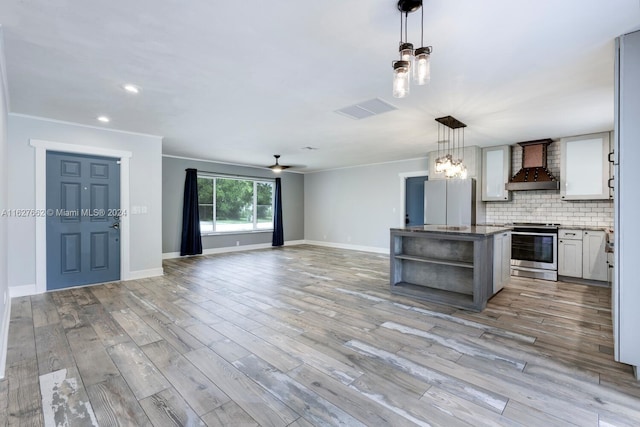 kitchen featuring hanging light fixtures, stainless steel stove, light wood-type flooring, and wall chimney exhaust hood