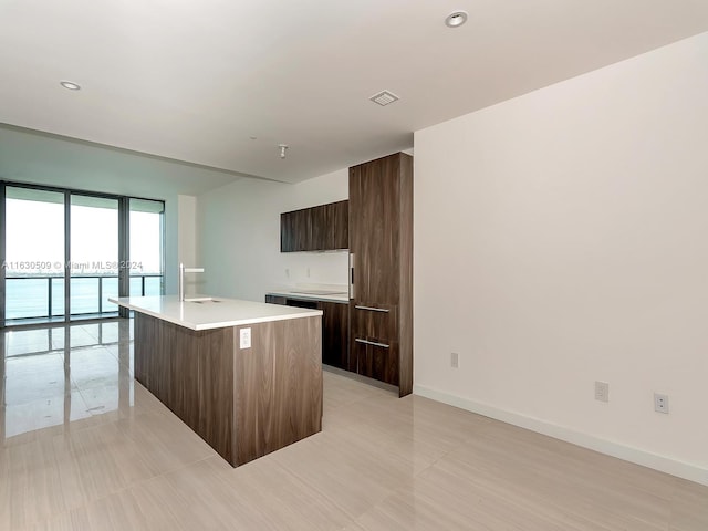 kitchen featuring floor to ceiling windows, sink, dark brown cabinets, light tile patterned floors, and a kitchen island