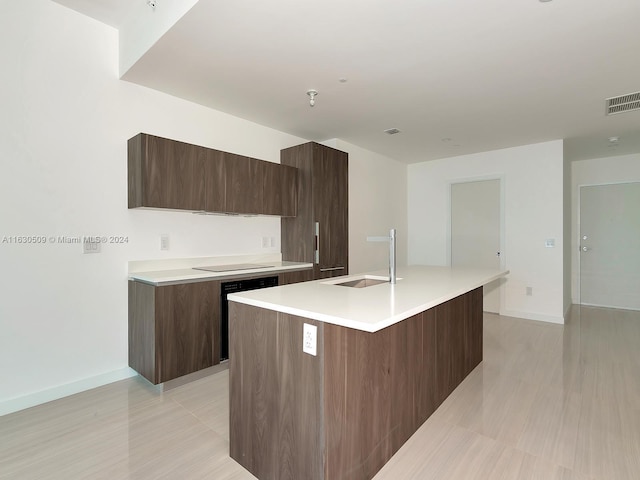 kitchen with black electric cooktop, sink, an island with sink, and dishwasher