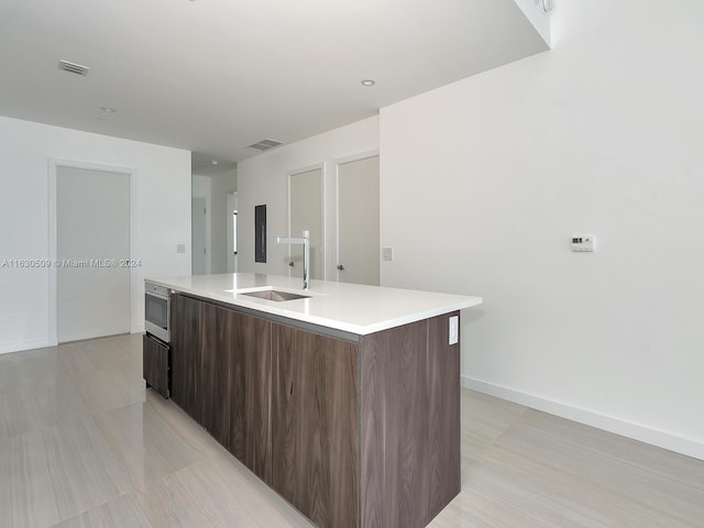 kitchen featuring a kitchen island with sink, sink, dark brown cabinets, and stainless steel microwave