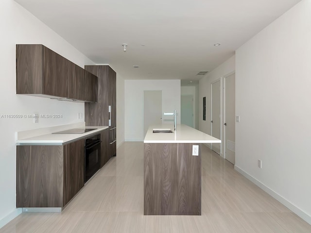 kitchen featuring a kitchen island with sink, sink, black appliances, and dark brown cabinetry