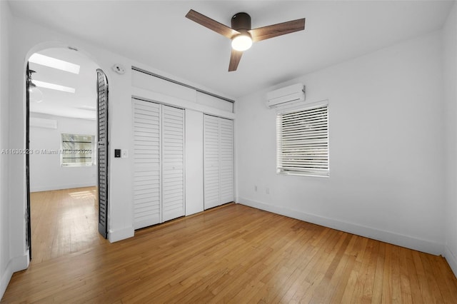 unfurnished bedroom featuring light hardwood / wood-style floors, a wall mounted air conditioner, and ceiling fan