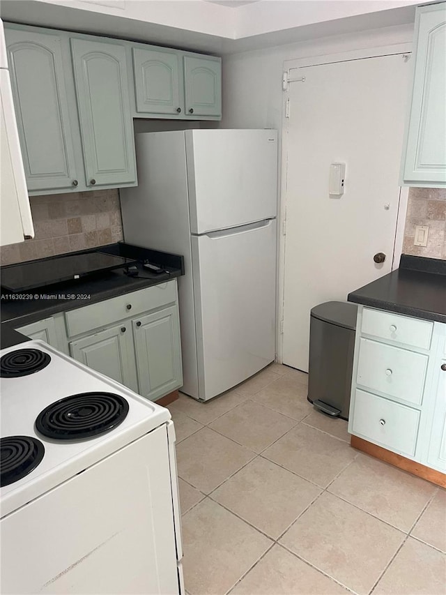 kitchen with white refrigerator, light tile patterned floors, range, and decorative backsplash