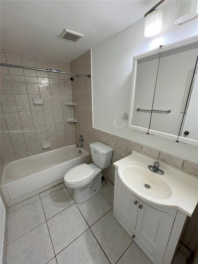 full bathroom with tiled shower / bath, toilet, vanity, tile walls, and tile patterned floors