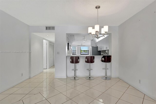 kitchen with pendant lighting, a breakfast bar area, stainless steel refrigerator, a notable chandelier, and kitchen peninsula