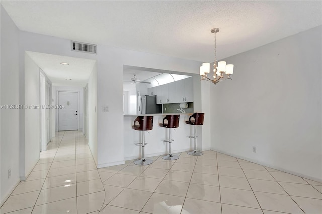 kitchen featuring stainless steel fridge, a kitchen breakfast bar, light tile patterned floors, kitchen peninsula, and a textured ceiling