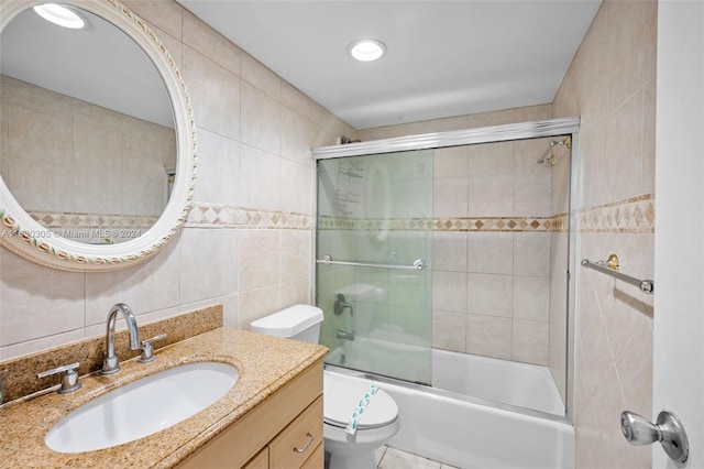 full bathroom with bath / shower combo with glass door, toilet, vanity, tile walls, and tile patterned floors