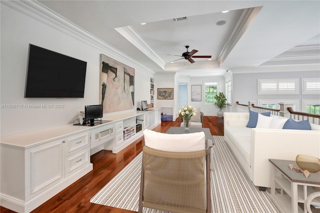 living room with a raised ceiling, crown molding, built in desk, and light wood-type flooring