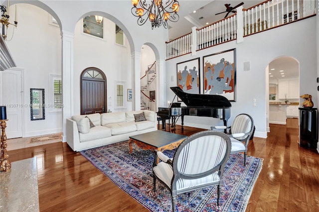 living room featuring dark wood-type flooring, a towering ceiling, a notable chandelier, and ornate columns