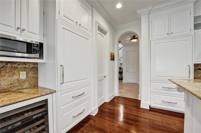 kitchen featuring dark hardwood / wood-style floors, white cabinetry, wine cooler, light stone counters, and crown molding