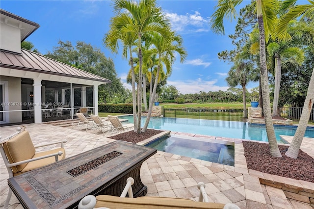 view of pool featuring a water view, a patio, an in ground hot tub, a fire pit, and a sunroom