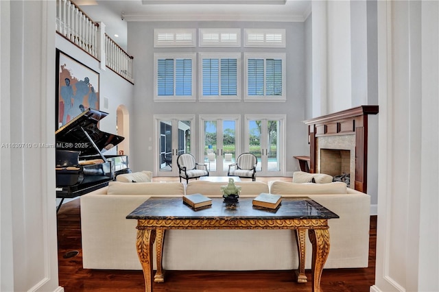 living room featuring french doors, dark wood-type flooring, crown molding, a towering ceiling, and a premium fireplace