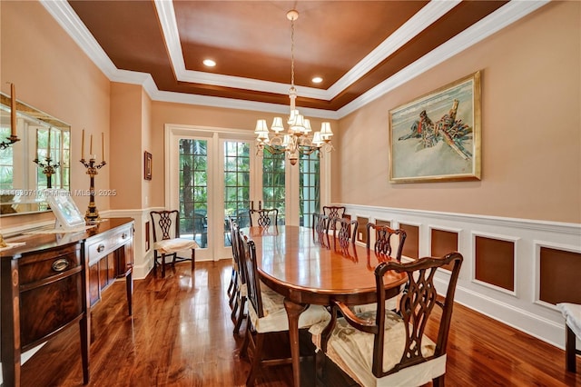 dining space with crown molding, dark wood-type flooring, a notable chandelier, and a tray ceiling