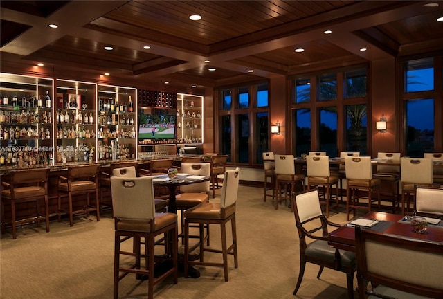 interior space featuring bar, coffered ceiling, light carpet, and wooden ceiling