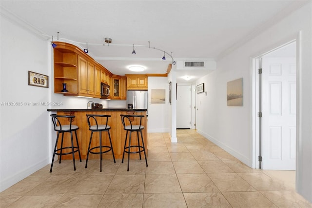 kitchen with appliances with stainless steel finishes, kitchen peninsula, light tile patterned flooring, and a breakfast bar