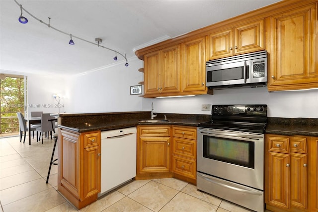 kitchen featuring light tile patterned floors, brown cabinetry, a peninsula, a sink, and appliances with stainless steel finishes