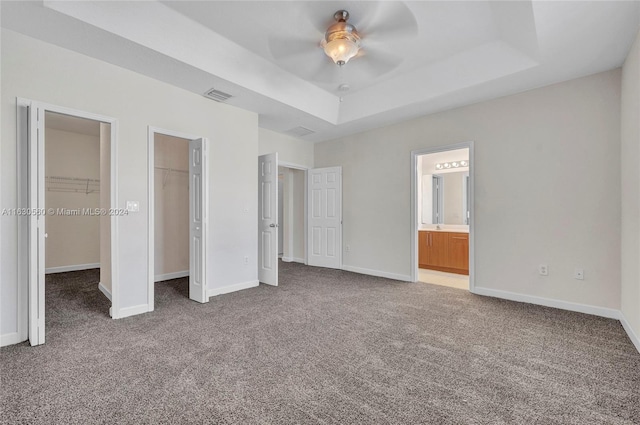 unfurnished bedroom with ensuite bath, ceiling fan, a raised ceiling, and carpet flooring