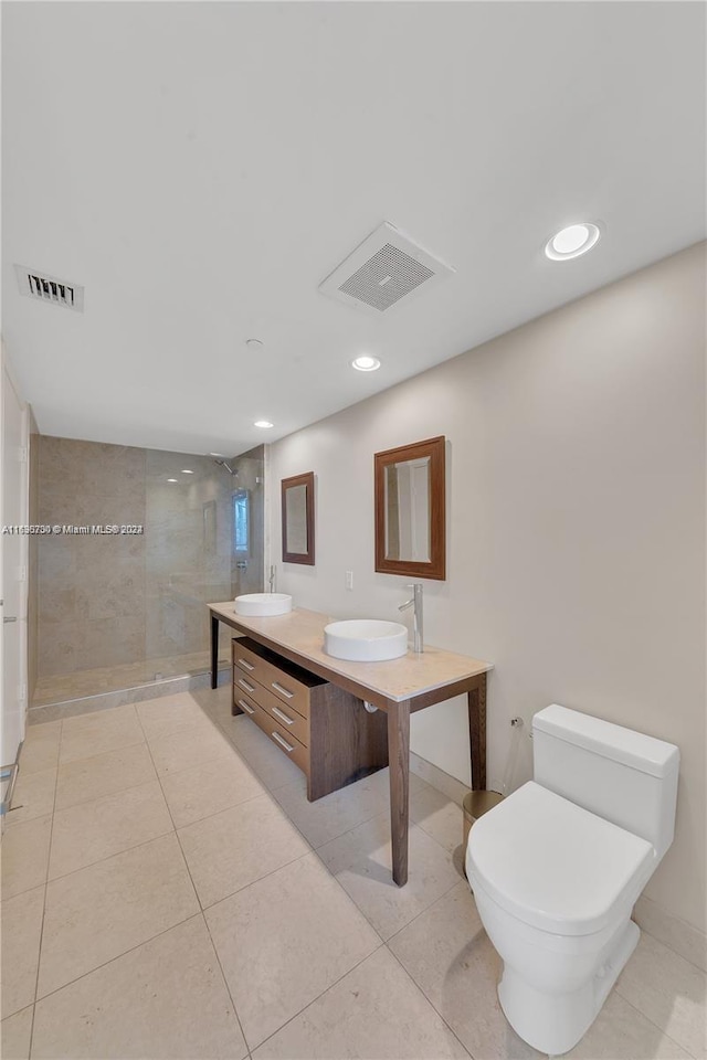 bathroom with tile patterned flooring, vanity, a tile shower, and toilet