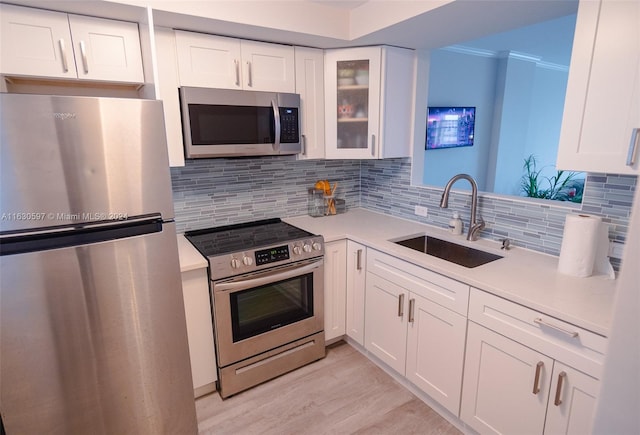 kitchen with light hardwood / wood-style floors, stainless steel appliances, ornamental molding, sink, and white cabinetry