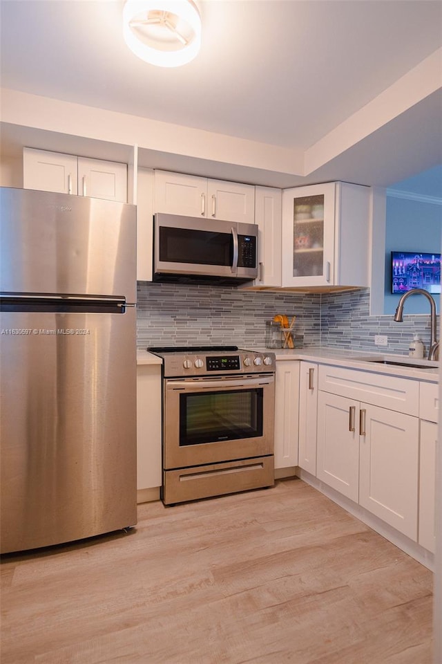 kitchen featuring appliances with stainless steel finishes, tasteful backsplash, light hardwood / wood-style floors, sink, and white cabinetry