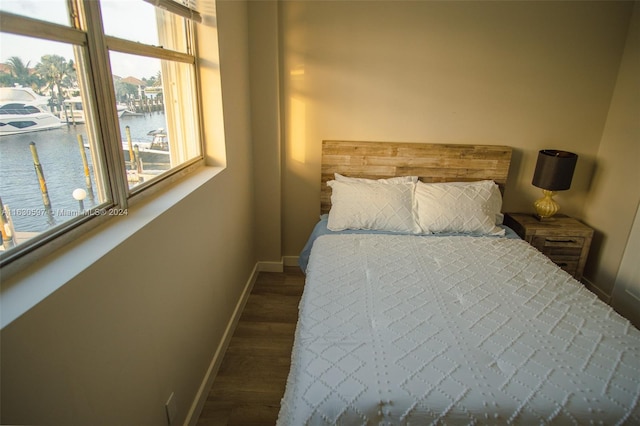 bedroom with dark hardwood / wood-style flooring and a water view