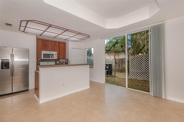 kitchen with decorative backsplash, stainless steel fridge, a tray ceiling, sink, and range