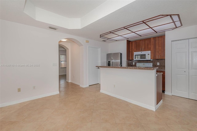 kitchen with arched walkways, tasteful backsplash, visible vents, white microwave, and stainless steel fridge with ice dispenser