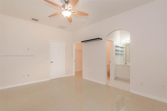 unfurnished room with arched walkways, ceiling fan, baseboards, and light tile patterned floors