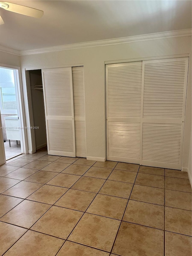 unfurnished bedroom featuring crown molding, light tile patterned floors, multiple closets, and ceiling fan