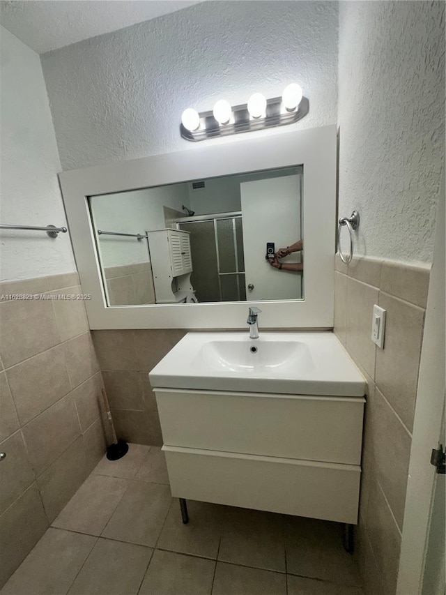 bathroom with a shower with door, a textured ceiling, tile walls, tile patterned floors, and vanity