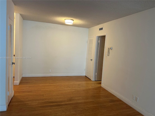 unfurnished room featuring a textured ceiling, baseboards, visible vents, and wood finished floors