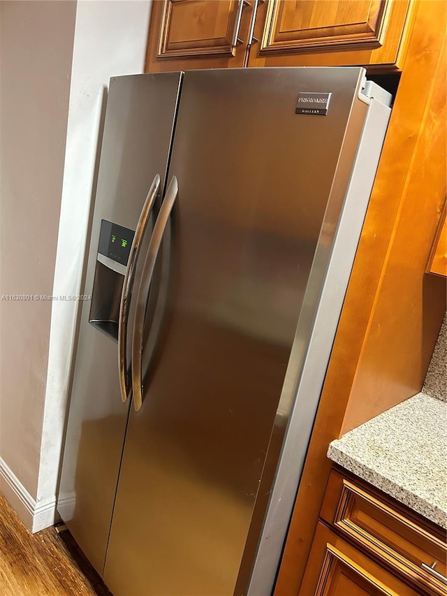 details with brown cabinetry, wood finished floors, light stone counters, stainless steel fridge, and baseboards