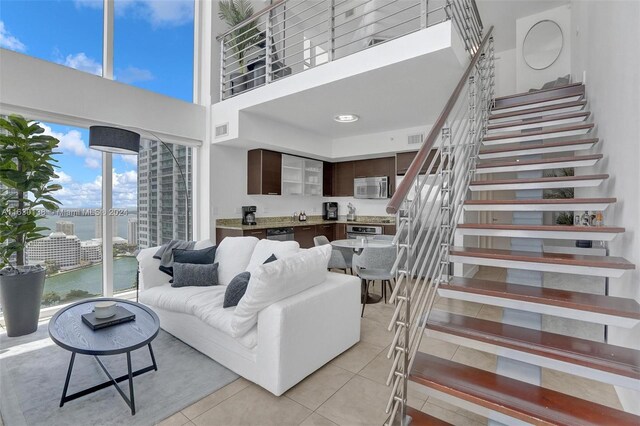 tiled living room featuring a healthy amount of sunlight, a water view, and a towering ceiling