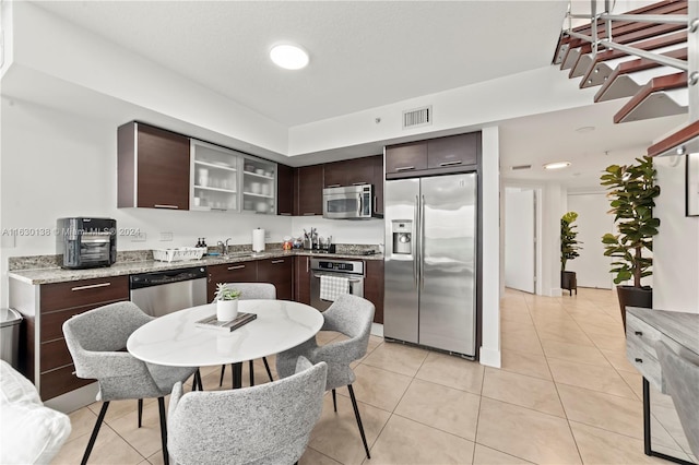 kitchen with dark brown cabinets, sink, light stone counters, light tile patterned flooring, and stainless steel appliances